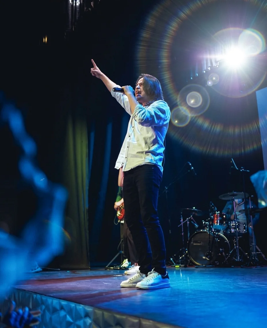 David cantando en el escenario con el brazo elevado bajo iluminación azul